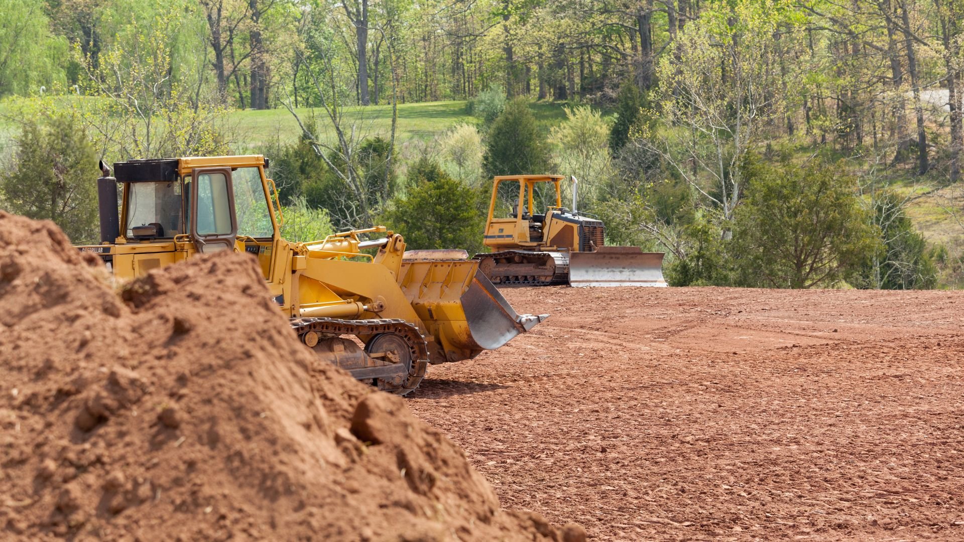 Yellow bulldozers clearing dirt on construction site surrounded by trees