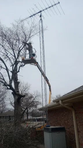 Worker on lift installing large antenna on roof near bare trees